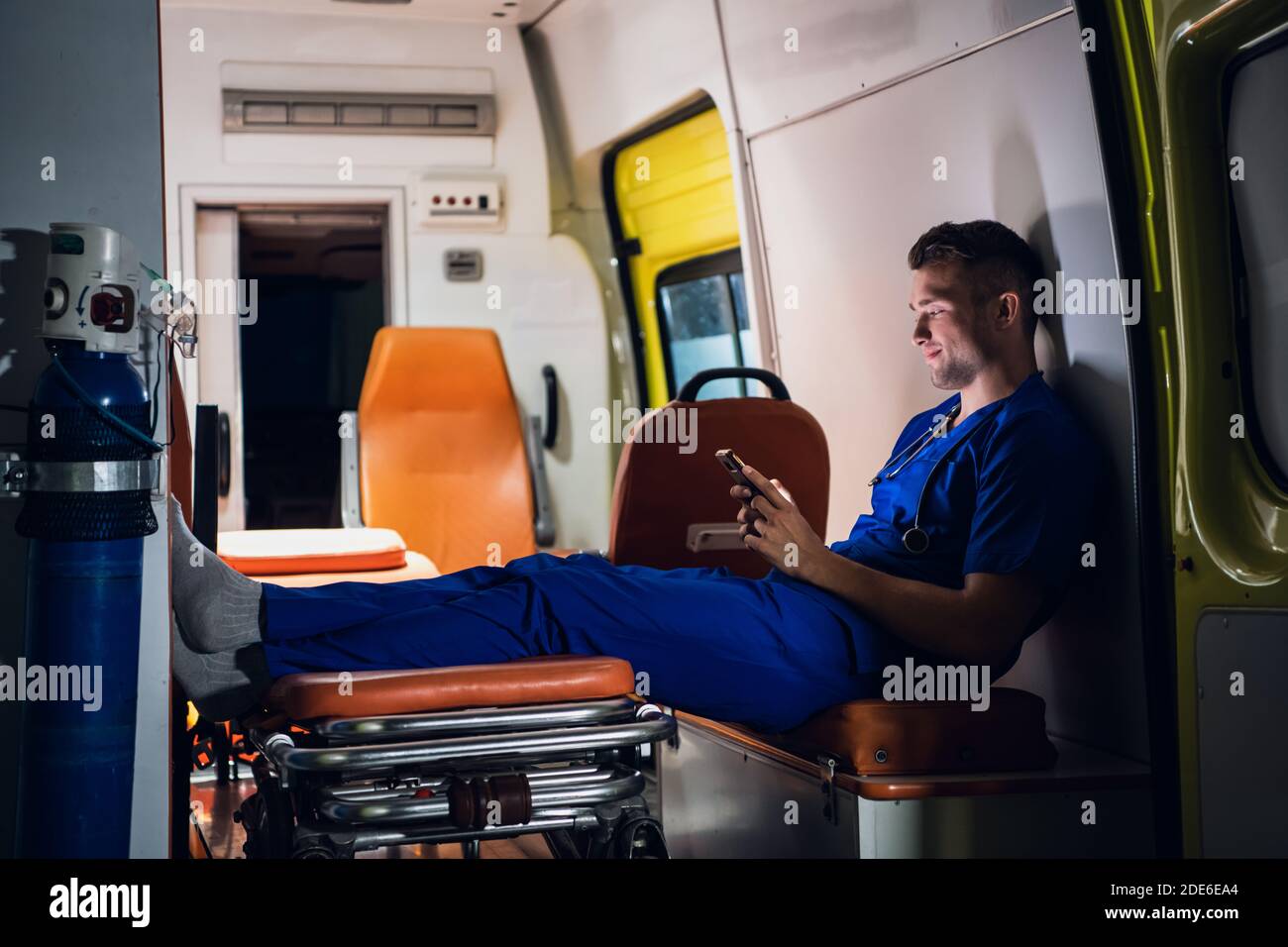 Jeune médecin dans un uniforme bleu textant à quelqu'un la nuit. Banque D'Images