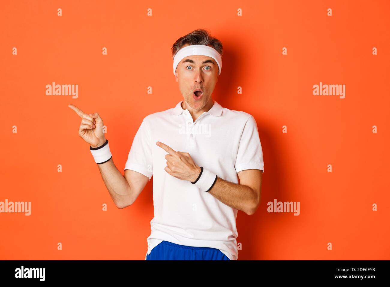 Portrait d'un homme d'âge moyen surpris faisant du sport, montrant quelque chose d'étonnant, pointant les doigts vers la gauche et regardant fasciné, portant des vêtements d'activité pour Banque D'Images