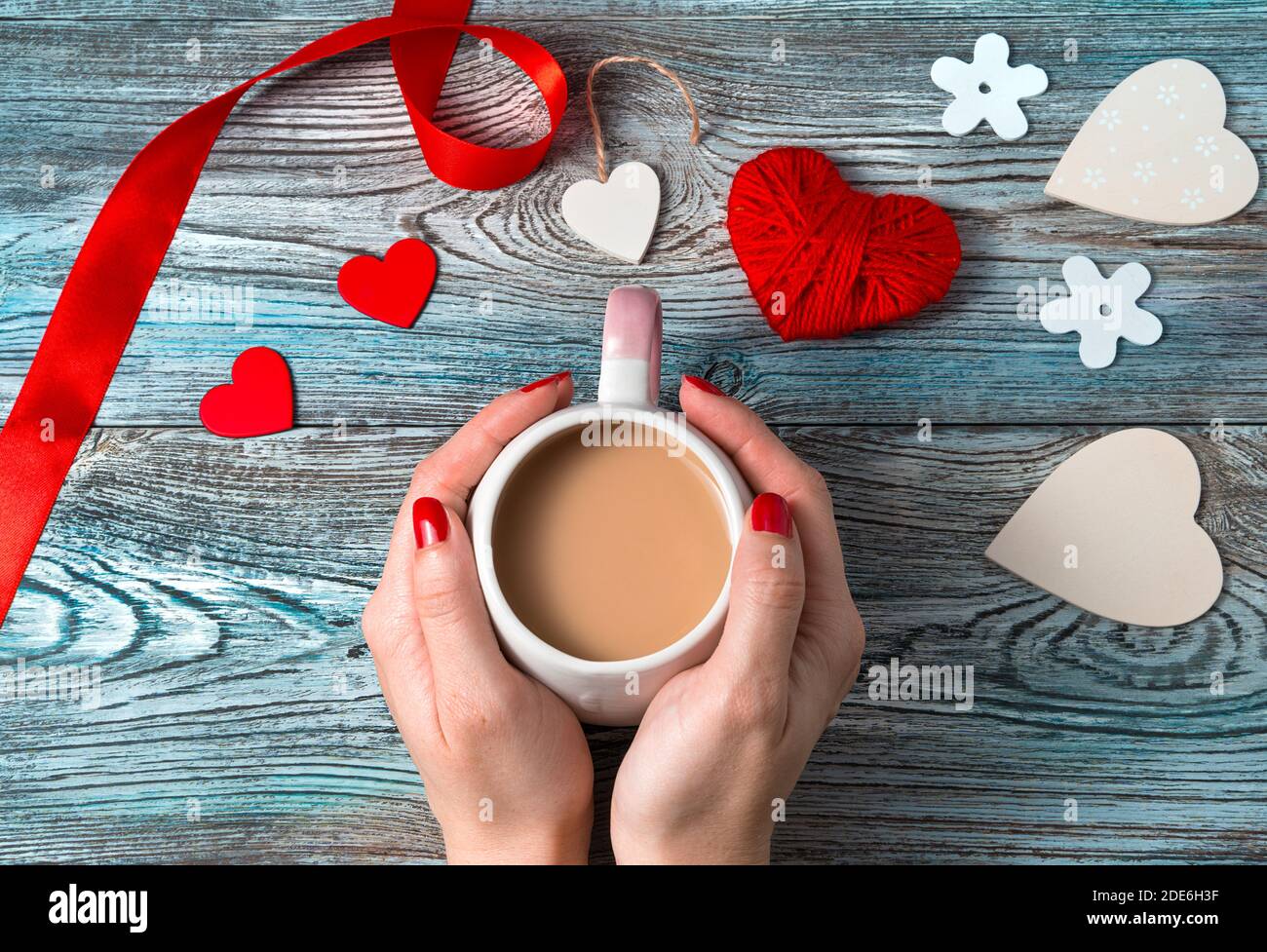 Mains d'une femme tenant une tasse de café avec du lait sur un fond romantique. Banque D'Images