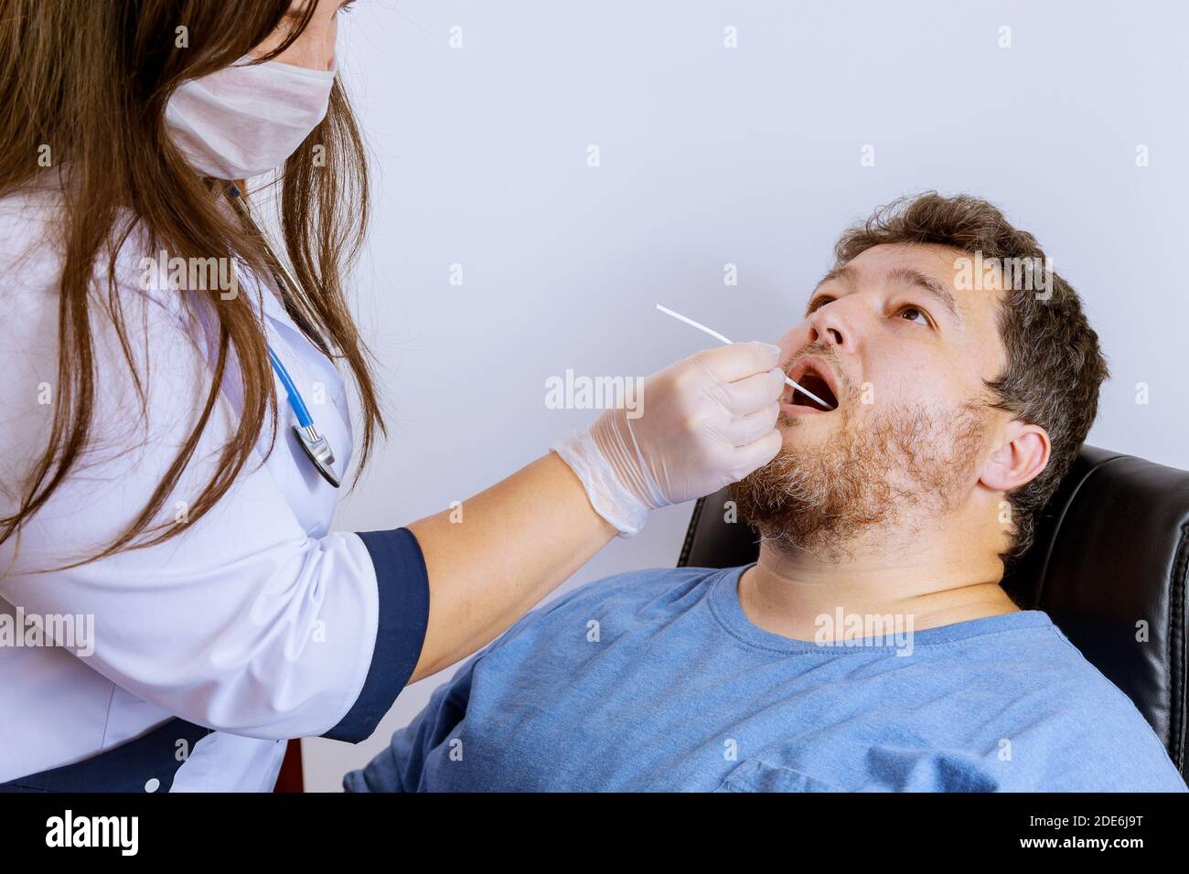 Un travailleur de la santé qui a de l'équipement effectue un écouvillon de coronavirus sur un écouvillon de bouche d'homme pour le coronavirus COVID-19. Banque D'Images