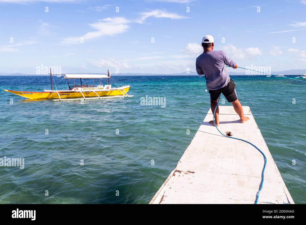 Un marin philippin tirant sur une corde pour amarrer son bateau-stabilisateur au large de la ville de Baclayon à Bohol, Philippines Banque D'Images