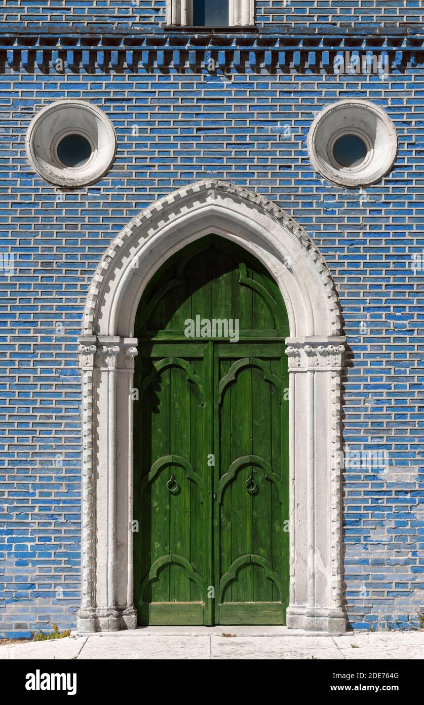 Façade extérieure d'un bâtiment historique gothique avec un vert porte en bois et mur en brique de couleur bleue Banque D'Images