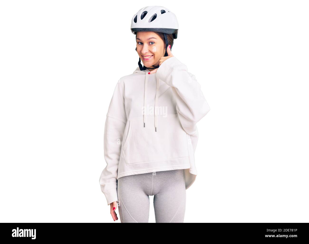Belle brune jeune femme portant un casque de vélo et des vêtements sportifs souriant faisant le téléphone geste avec la main et les doigts comme parler au téléphone. Banque D'Images