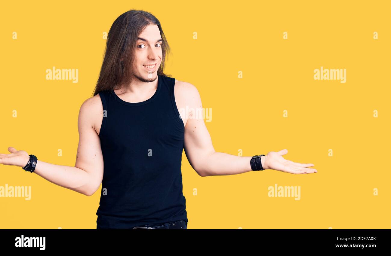 Jeune homme adulte avec de longs cheveux portant le style goth avec des vêtements noirs souriant montrant les deux mains ouvertes paumes, présentation et publicité comparaison et Banque D'Images