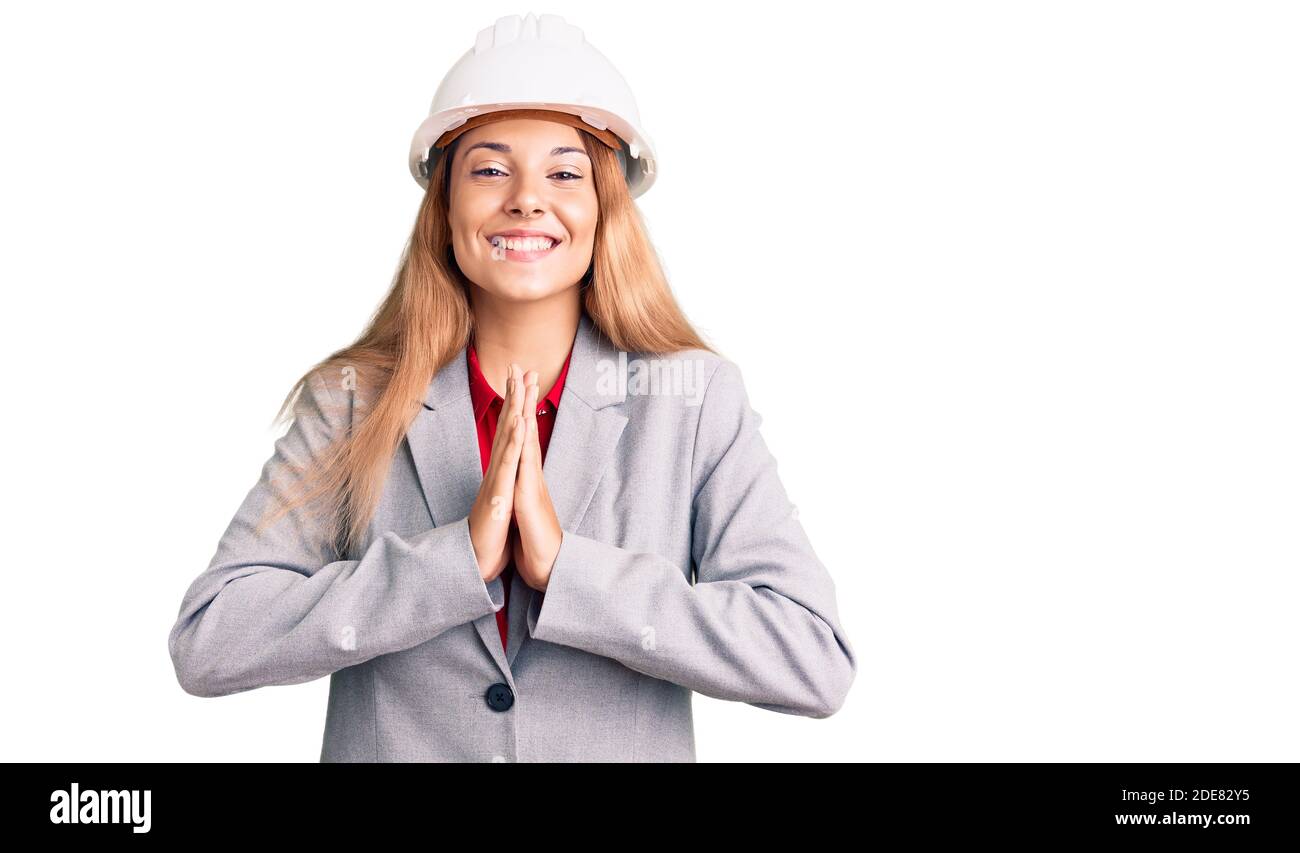 Belle jeune femme portant le casque d'architecte priant avec les mains ensemble demandant pardon souriant confiant. Banque D'Images