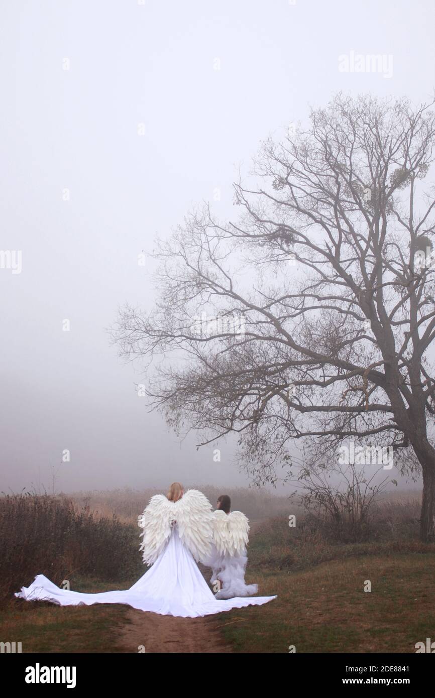 Deux filles en costumes d'ange et robes blanches marchant dans le parc. Mère et fille Banque D'Images