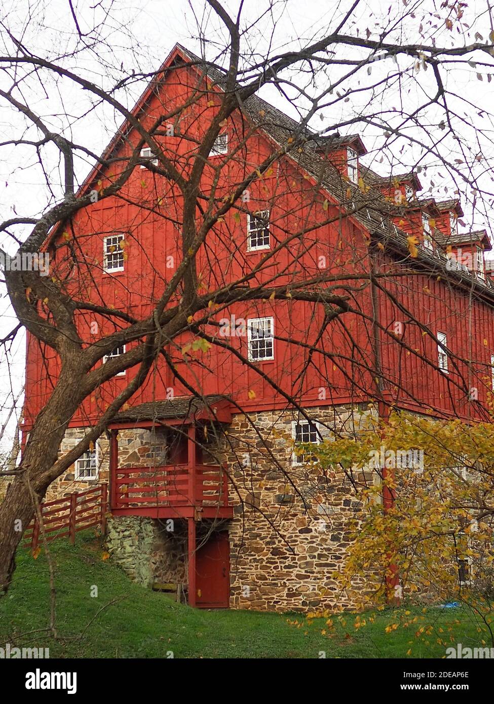 Une belle maison de moulin à la fin des années 1700 le bois peint en pierre et rouge est niché dans une pelouse hill un jour d'hiver derrière bare tree bran Banque D'Images