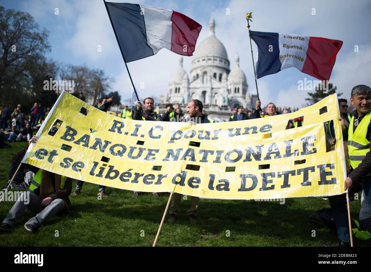 Les manifestants de la Yellow Vest se réunissent devant la basilique du Sacré-cœur à Montmartre. Les manifestants détiennent deux drapeaux français et une pancarte pour le R.I.C., arbitre d'initiative citadine à Paris, le 23 mars 2019, lors d'une manifestation antigouvernementale organisée par le mouvement de la « Yellow Vest » (gilets jaunes). Les manifestants ont de nouveau frappé les rues de la ville française le 23 mars, pour une 19e semaine consécutive de protestation nationale ( Loi 19 ) contre la politique du président français et son style de gouvernement descendant, le coût élevé de la vie, les réformes fiscales gouvernementales et pour une plus grande « justice sociale et économique. » photo de Raphaël Banque D'Images