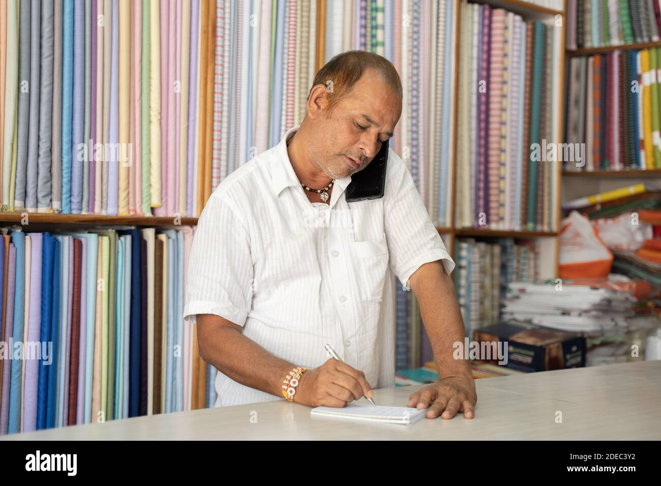 Commerçant prenant la commande sur le téléphone mobile à magasin de tissu - concept de propriétaire de petite entreprise notant l'ordre, en utilisant la technologie et la communication. Banque D'Images