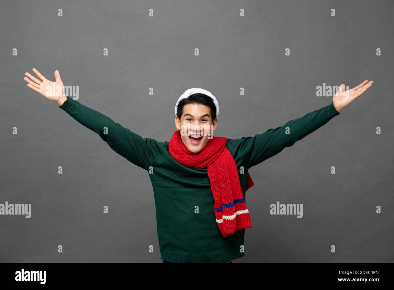 Joyeux jeune homme asiatique excité portant des vêtements à thème de Noël avec open arms gesture studio tourné isolé sur fond gris Banque D'Images