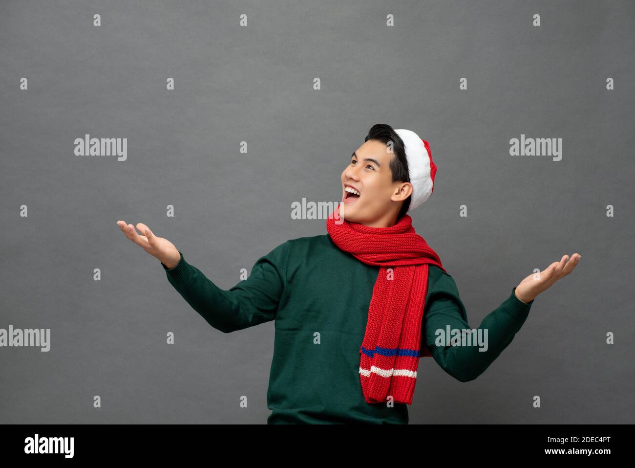 Un jeune homme asiatique amusant portant des vêtements de Noël ouverts les paumes se tournent vers l'espace vide de côté Banque D'Images