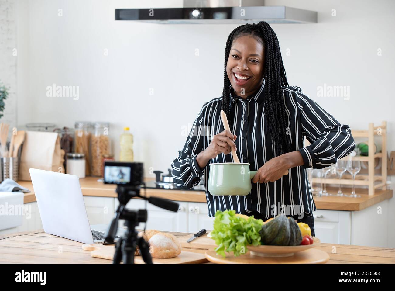 Bonne femme africaine américaine vlogger de diffusion de vidéo en direct en ligne pendant cuisine dans la cuisine à la maison Banque D'Images