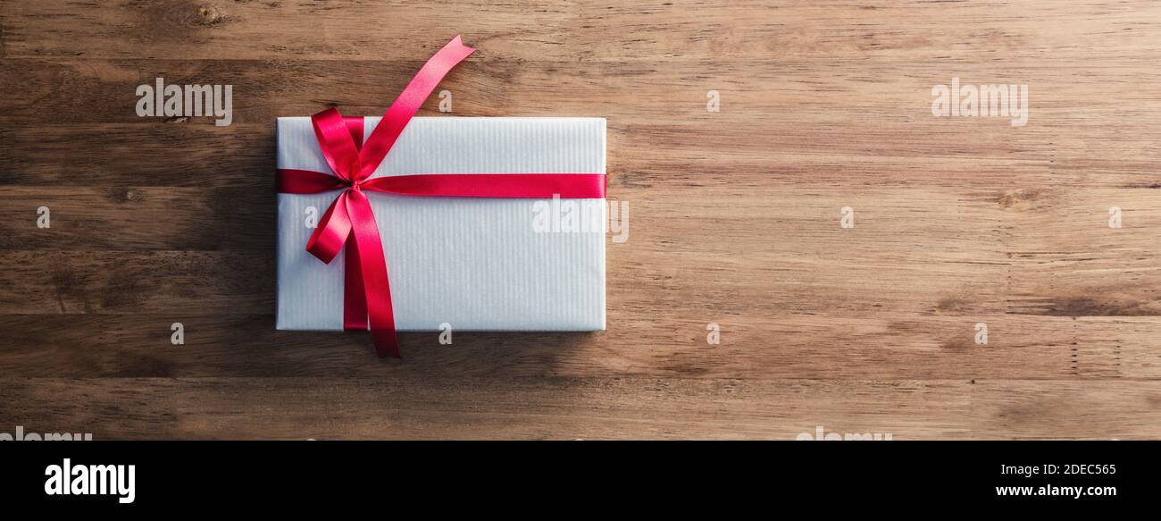 Boîte cadeau de Noël emballée de papier gris et de ruban rouge arc sur la bannière de table en bois vue de dessus avec copie espace Banque D'Images