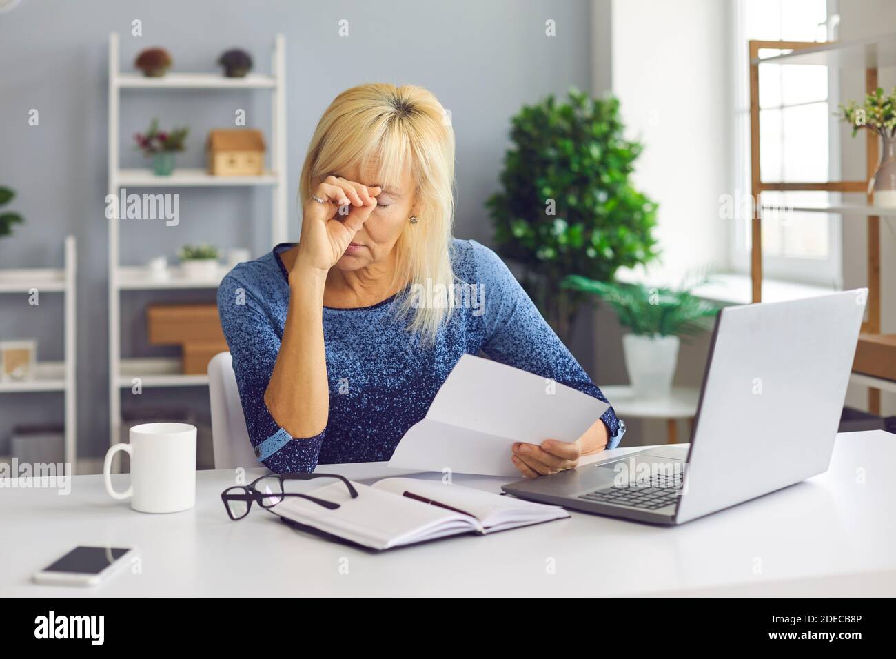 Contrarié femme séchée à son bureau, tenant une faillite ou un avis de dette de la banque Banque D'Images