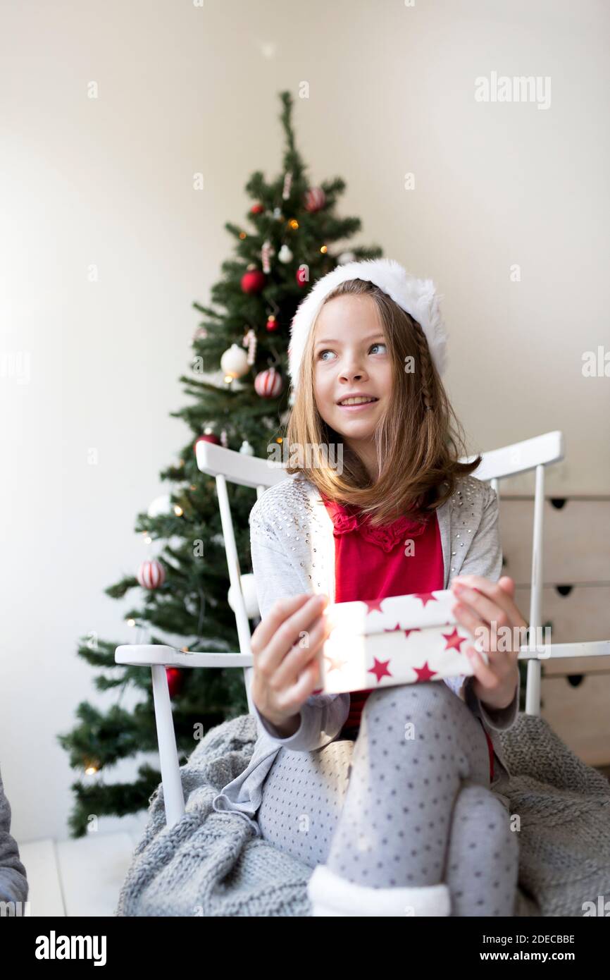 Jolie fille dans santa clause chapeau devant un Arbre de Noël avec cadeaux de Noël Banque D'Images