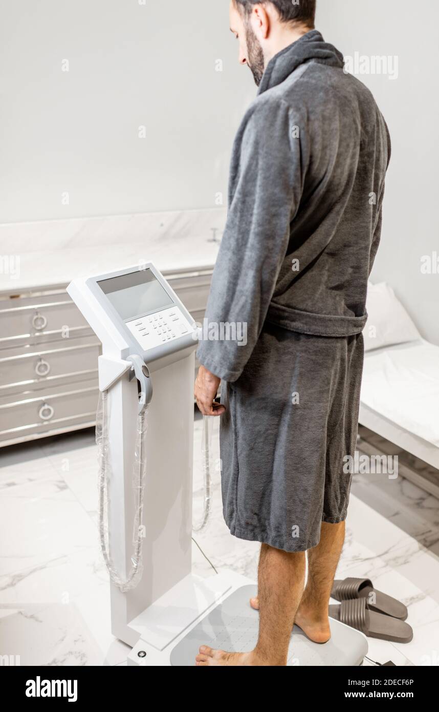 Homme mesurant l'équilibre de la composition corporelle, debout sur la balance médicale pendant l'essai de corps au salon de spa de luxe Banque D'Images