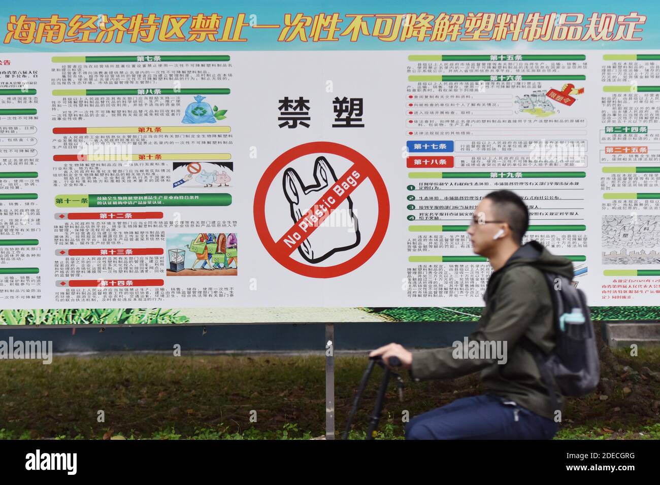 Haikou, Chine. 30 novembre 2020. Un étudiant d'université passe devant une affiche interdisant les sacs en plastique à Haikou.a partir du 1er décembre, le Hainan de Chine interdira la production, la vente et l'utilisation d'une large gamme de produits en plastique jetables, selon le département régional de l'écologie. Crédit : SOPA Images Limited/Alamy Live News Banque D'Images