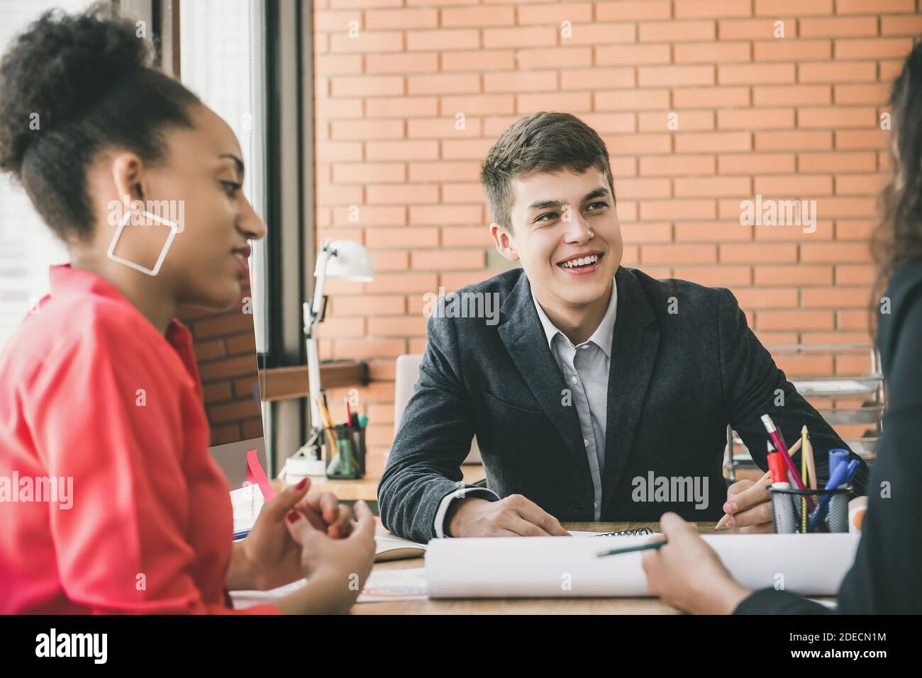 Jeune homme d'affaires souriant et femme d'affaires noire écoutant attentivement leur collègue à la réunion des finances Banque D'Images