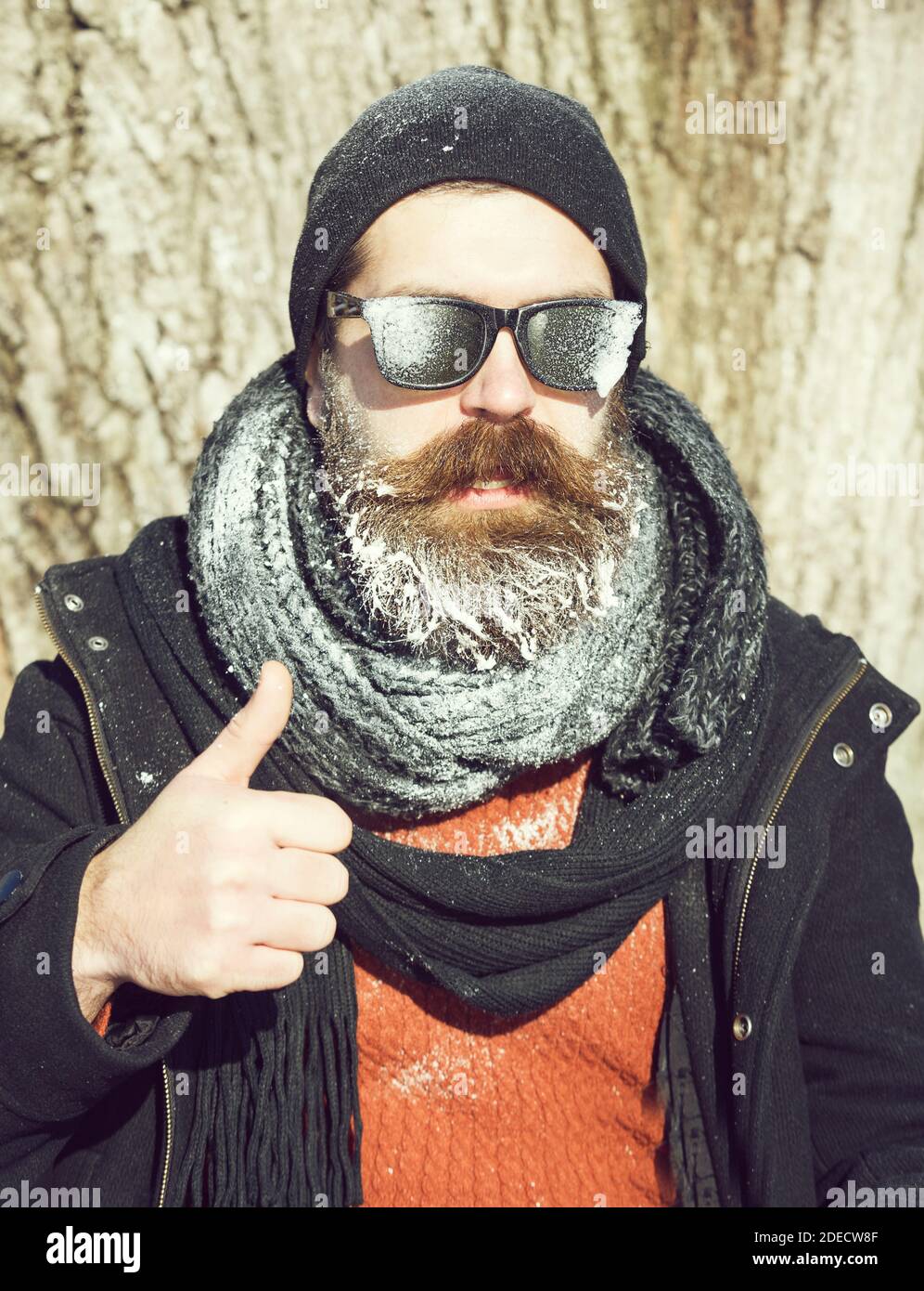 homme barbu, taille basse, avec barbe et moustache dans des lunettes de  soleil noires recouvertes de gel blanc donne un double pouce vers le haut  de geste pendant la journée d'hiver à