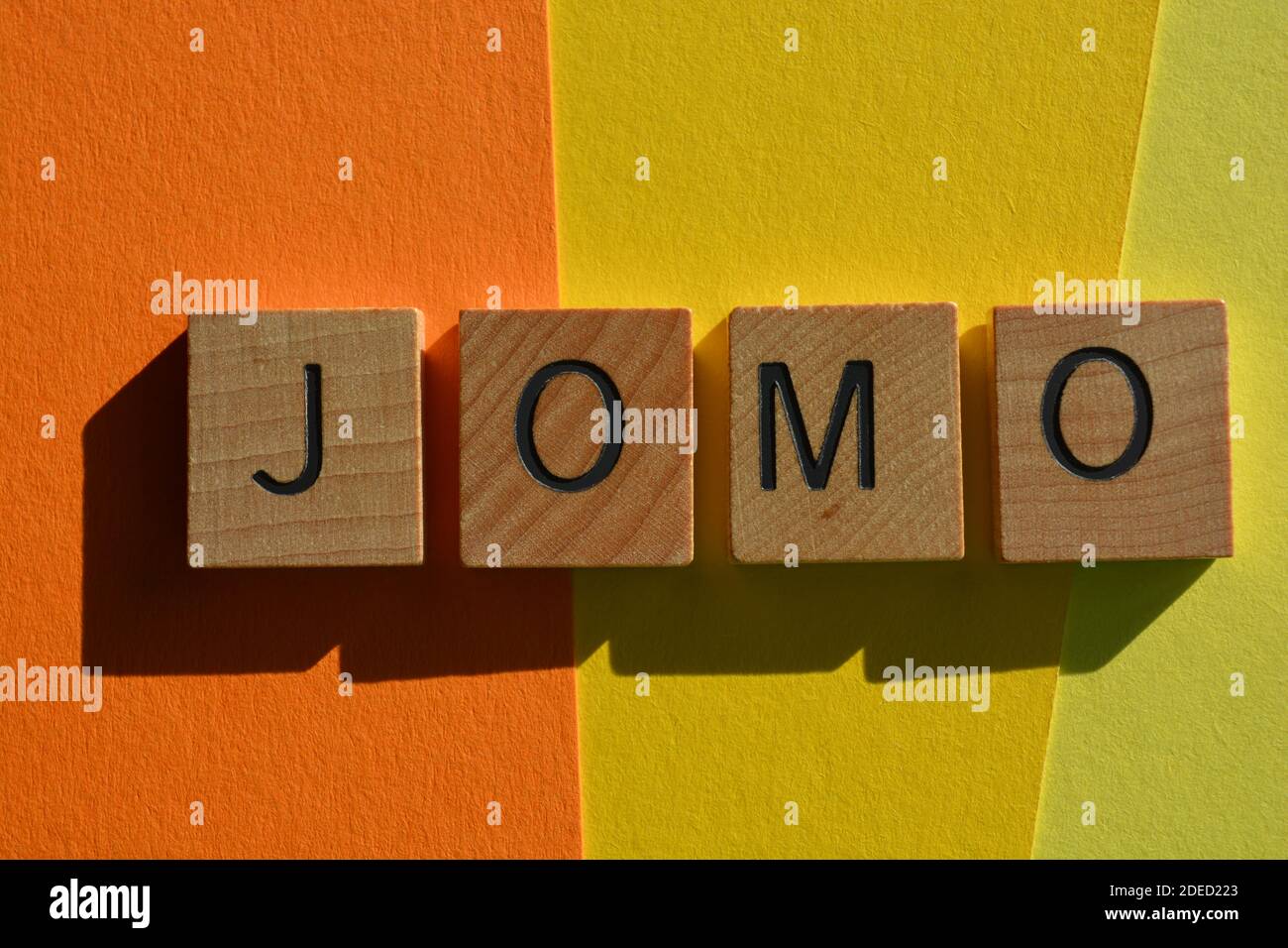 JOMO acronyme de Joy of Missing Out, en lettres de l'alphabet en bois isolées sur fond coloré Banque D'Images