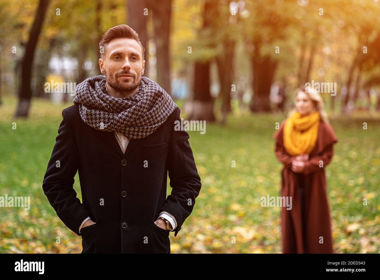 L'homme se tient dans un manteau et un foulard dans le parc en attendant sa  petite amie ou sa femme qui se tient derrière lui ou qui ressemble à lui de  l'arrière.