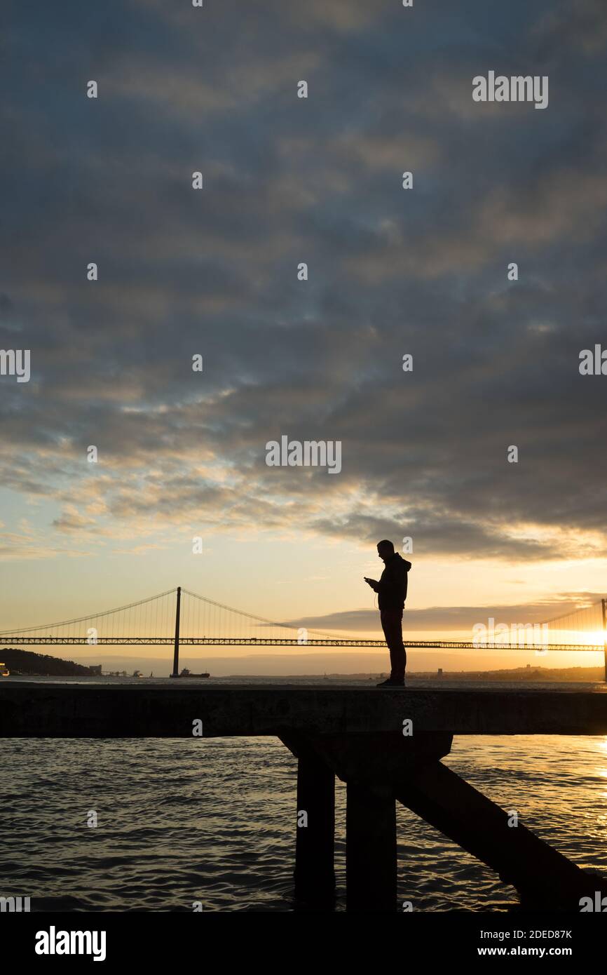 silhouette d'un homme regardant son téléphone sur un pont Banque D'Images