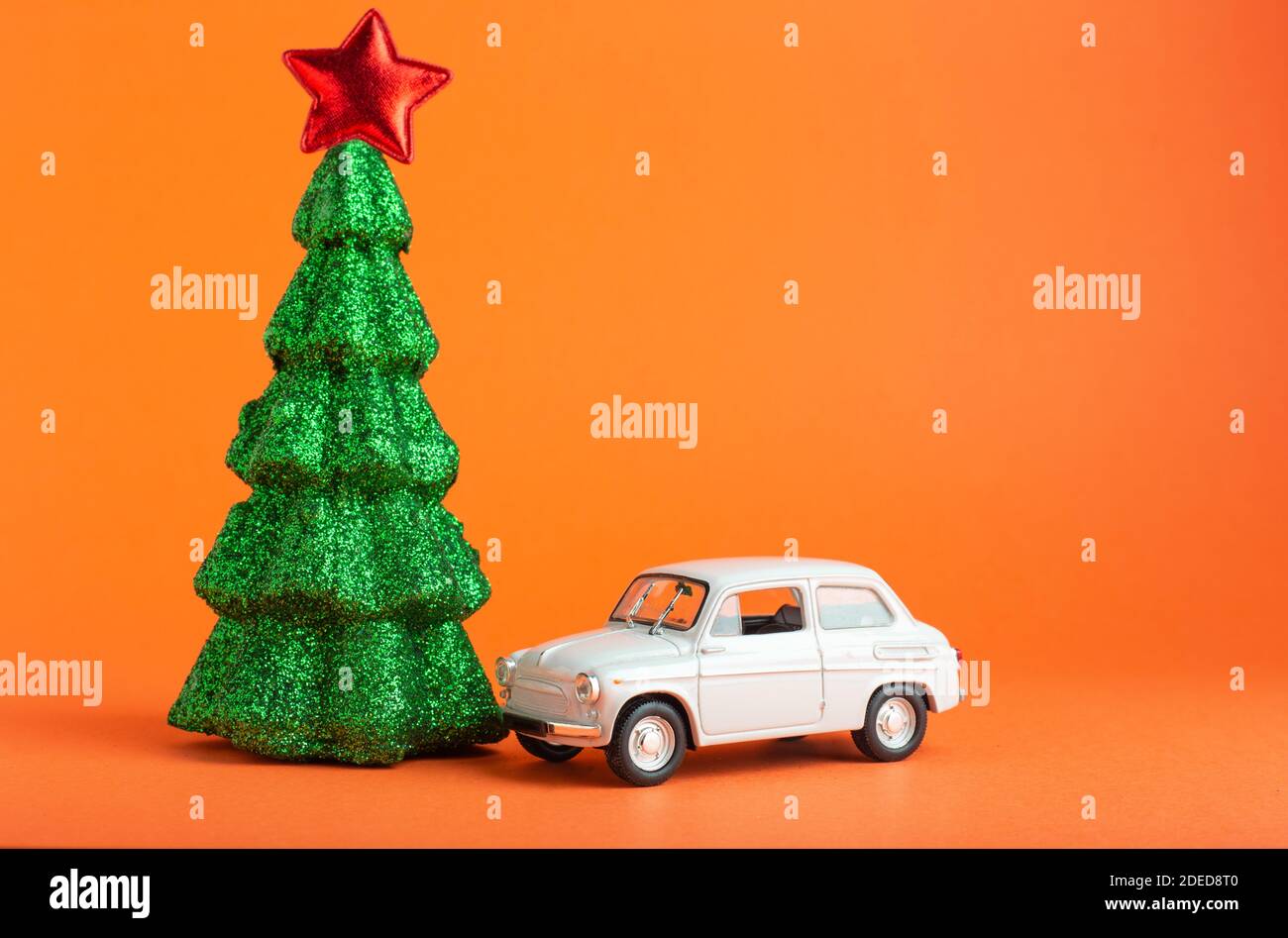 Arbre du nouvel an de Noël avec étoile rouge sur le dessus près du jouet de voiture blanc. Sapin de Noël miniature et voiture créatifs sur fond de couleur orange. Livraison de cadeaux Banque D'Images
