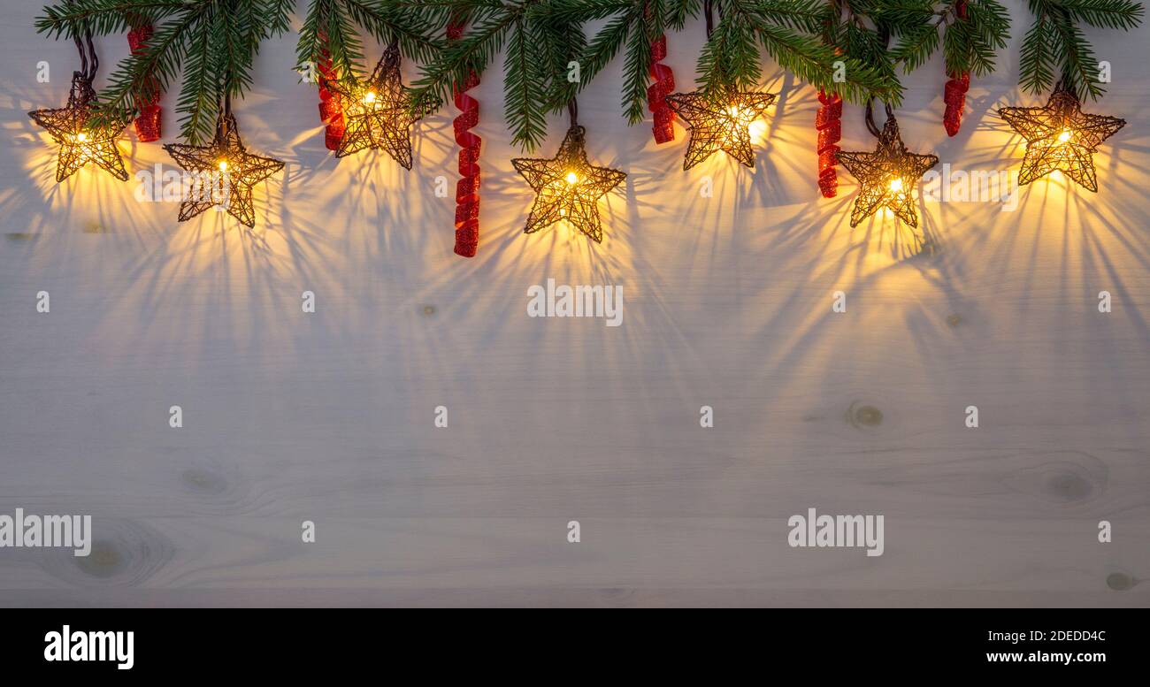 Lumières de Noël en forme d'étoile suspendues à la partie supérieure. Branches d'épicéa vert pour la décoration et cordes brillantes à boucles rouges. Espace de copie du lot. Banque D'Images