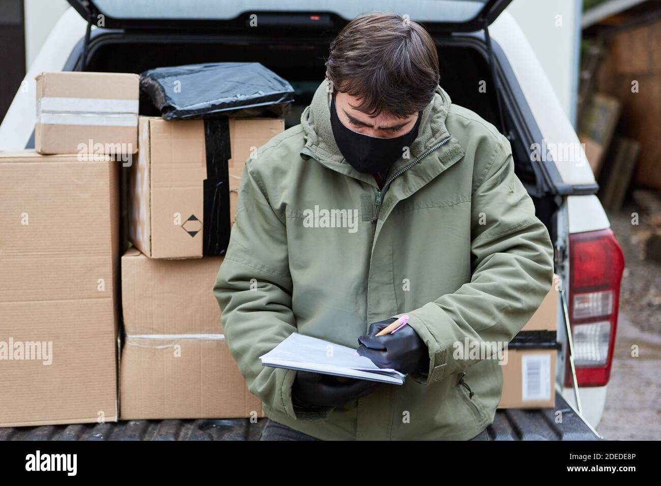 Le sous-traitant de service de colis apporte des colis dans la voiture avec le visage Masque en raison de Covid-19 pour Noël Banque D'Images