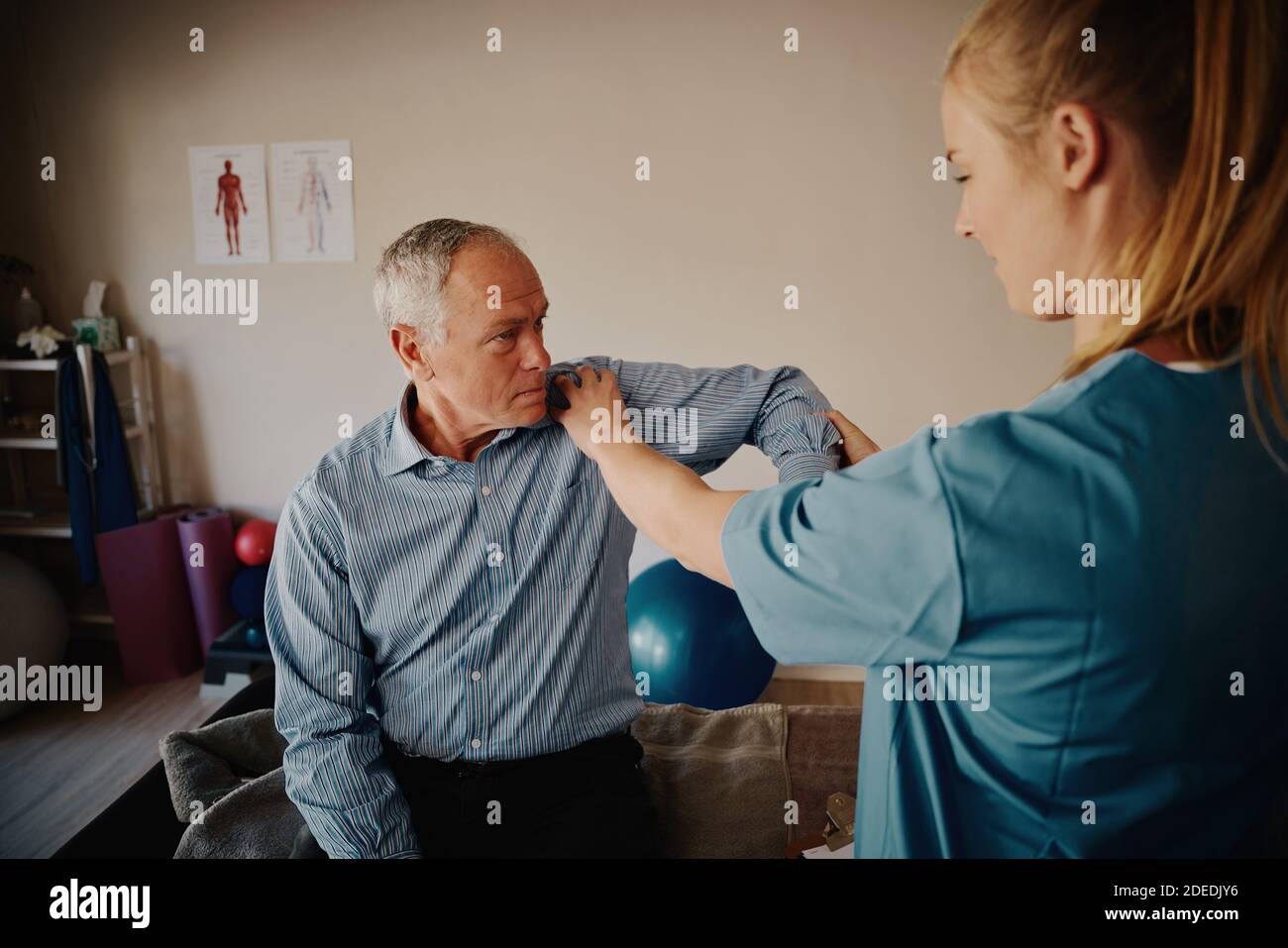 Jeune physiothérapeute femme examinant l'épaule et le coude d'un patient âgé dans la chambre d'hôpital Banque D'Images