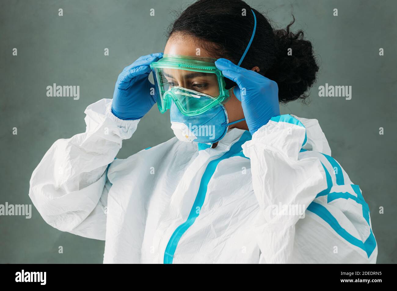 Jeune femme médic portant un costume de protection et un masque de mise sur les lunettes et en regardant vers le bas Banque D'Images