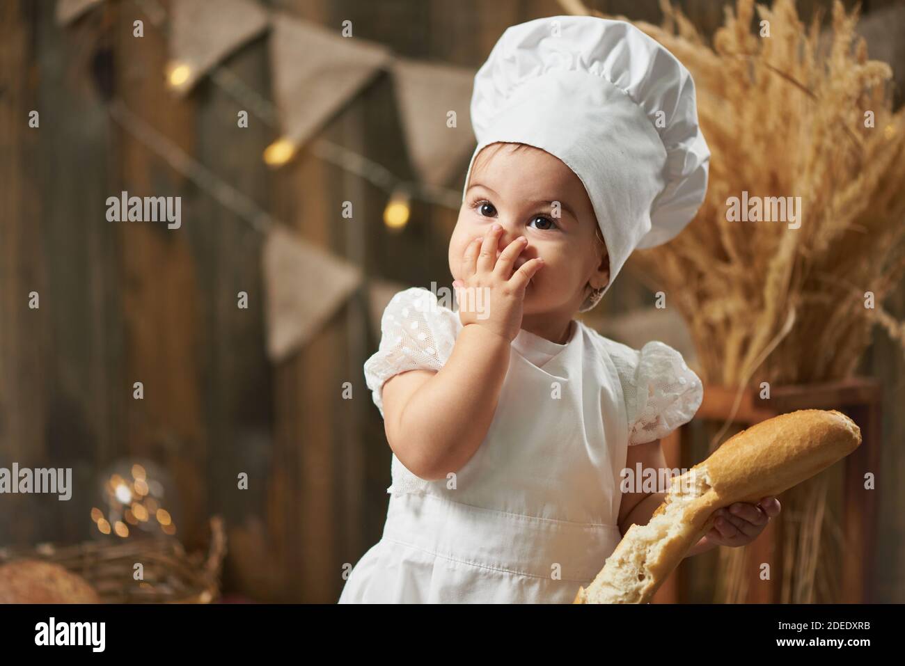 Une petite fille baker mange du pain et la ferme bouche Banque D'Images