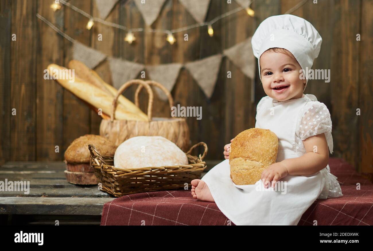 Adorable petit boulanger avec du pain frais sur le fond d'un mur en bois et du pain Banque D'Images