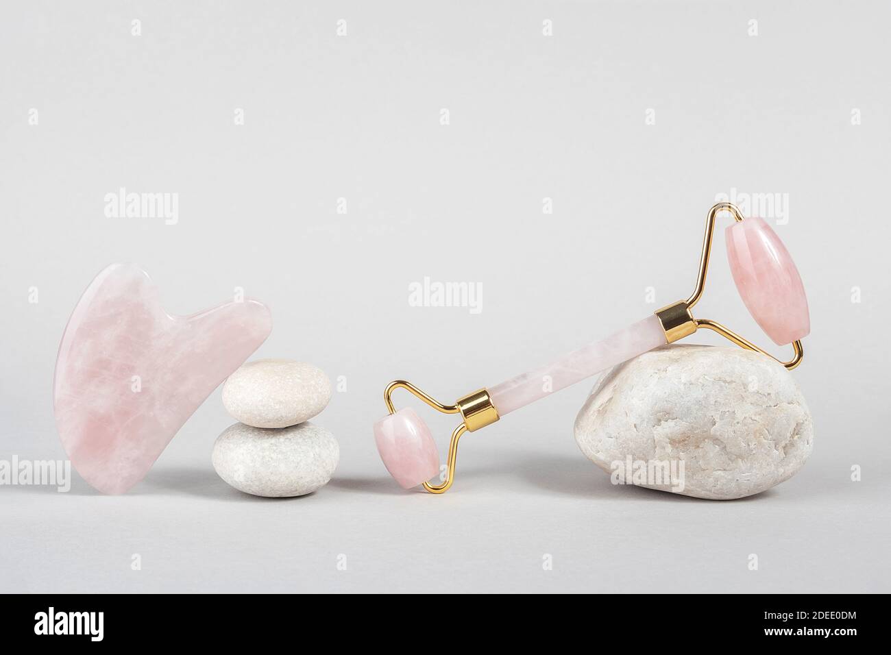 Rouleau facial en quartz rose cristal et outil de massage jade Gua sha sur pierres, fond gris. Massage facial anti-âge pour lever et tonifier votre visage Banque D'Images