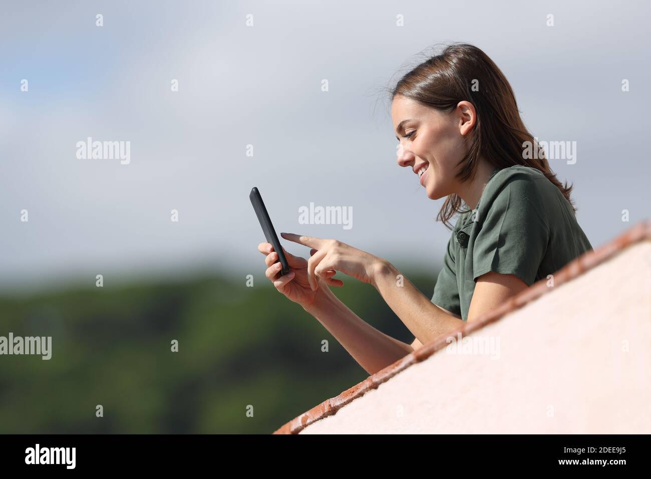 Femme heureuse dans un balcon d'appartement utilisant le smartphone A. journée ensoleillée en montagne Banque D'Images