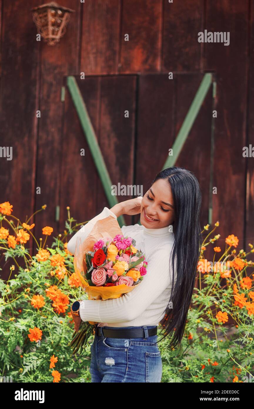 Une jeune femme heureuse tenant un bouquet de roses et debout à côté d'un bush plein de fleurs d'orange Banque D'Images