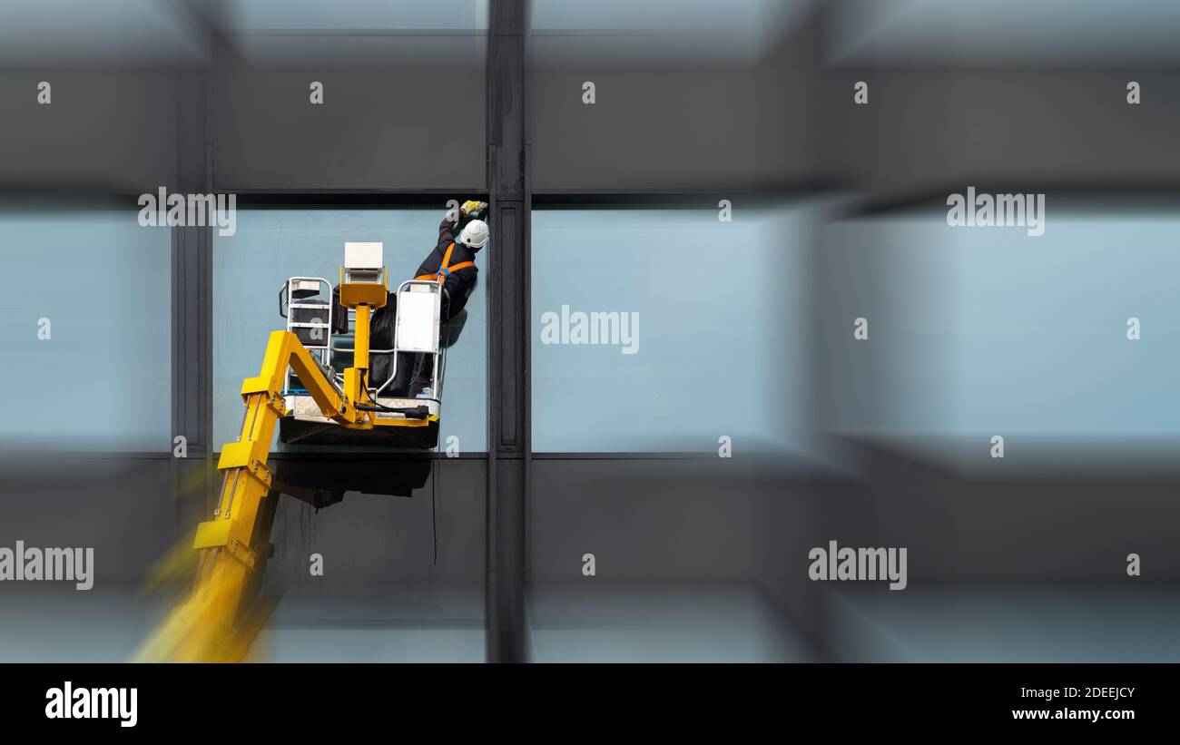 Homme nettoyant nettoyage vitre windows sur haut bâtiment moderne dans l'air sur une plate-forme de levage. Polissage du verre employé dans l'air élevée Banque D'Images