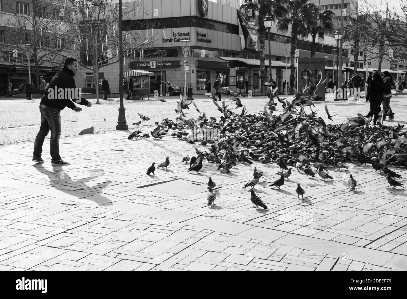 Izmir, Turquie - 12 février 2015 : l'homme nourrit des pigeons sur la place Konak, dans la partie centrale historique de la ville d'Izmir. Les gens ordinaires marchant sur le estre Banque D'Images