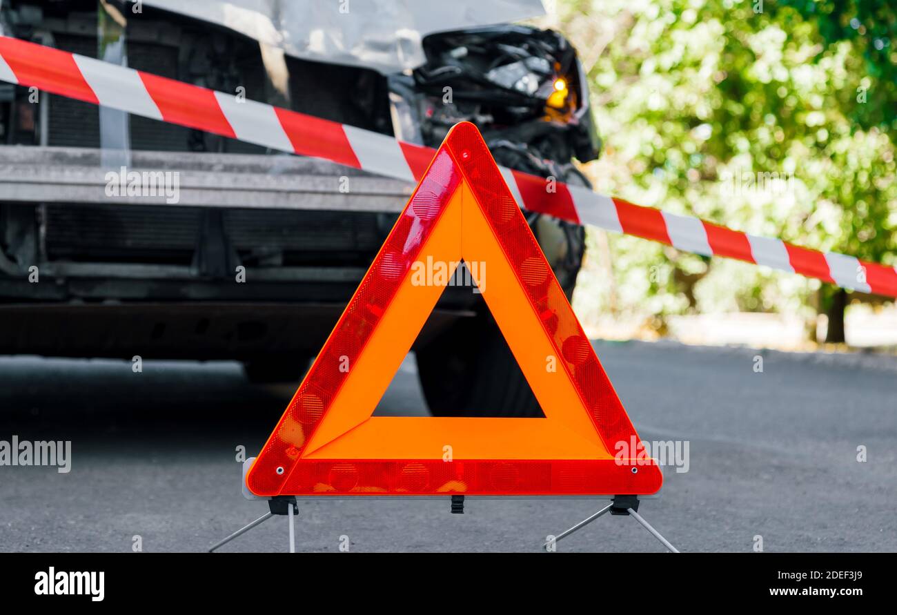 Triangle rouge d'arrêt d'urgence et ruban rouge blanc de police sur la route en face de l'accident de voiture. Véhicule utilitaire sport cassé dans un accident de la route. Accident de voiture Banque D'Images