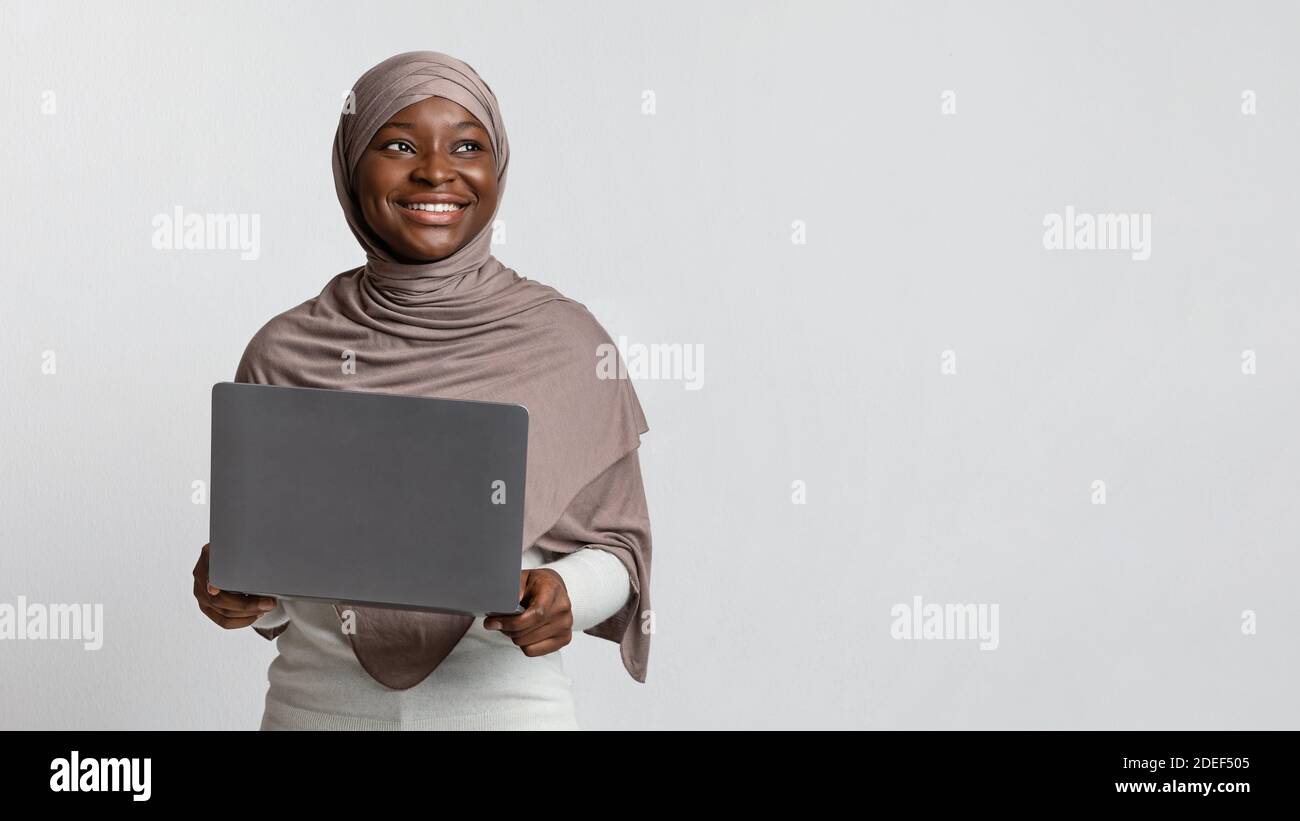 Carrière en ligne. Femme musulmane noire souriante rêveuse dans le hijab tenant un ordinateur portable Banque D'Images