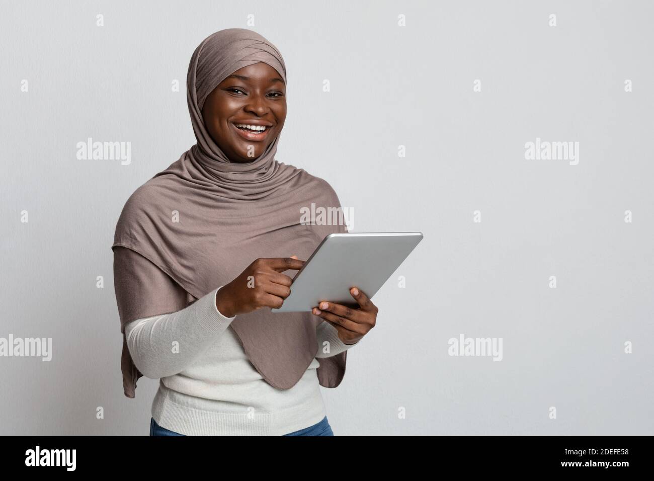 Une Black Lady souriante dans le hijab en utilisant la tablette numérique, en profitant des technologies modernes Banque D'Images