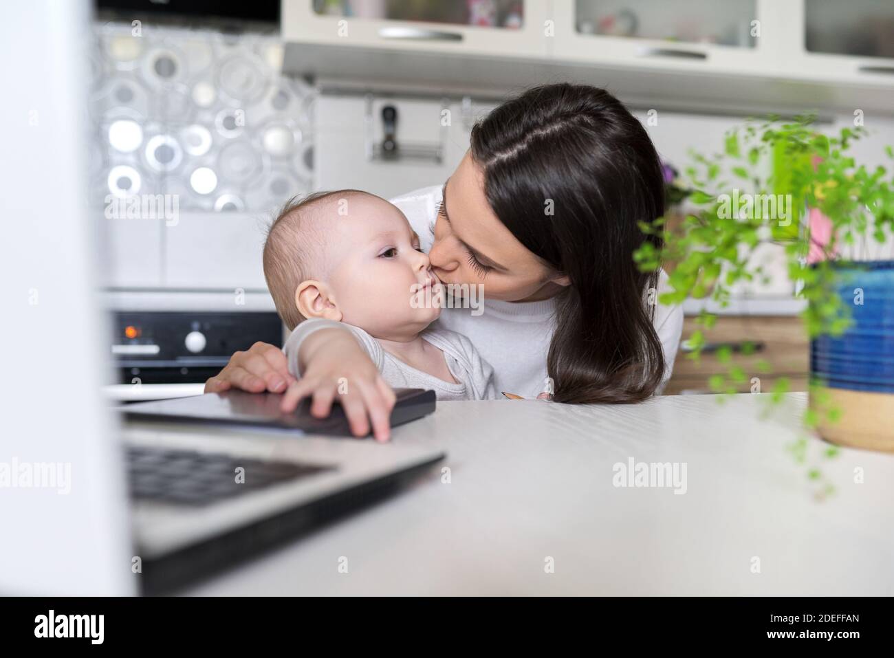 Portrait de mère et de bébé fils assis à la maison dans la cuisine, mère aimante embrassant bébé Banque D'Images