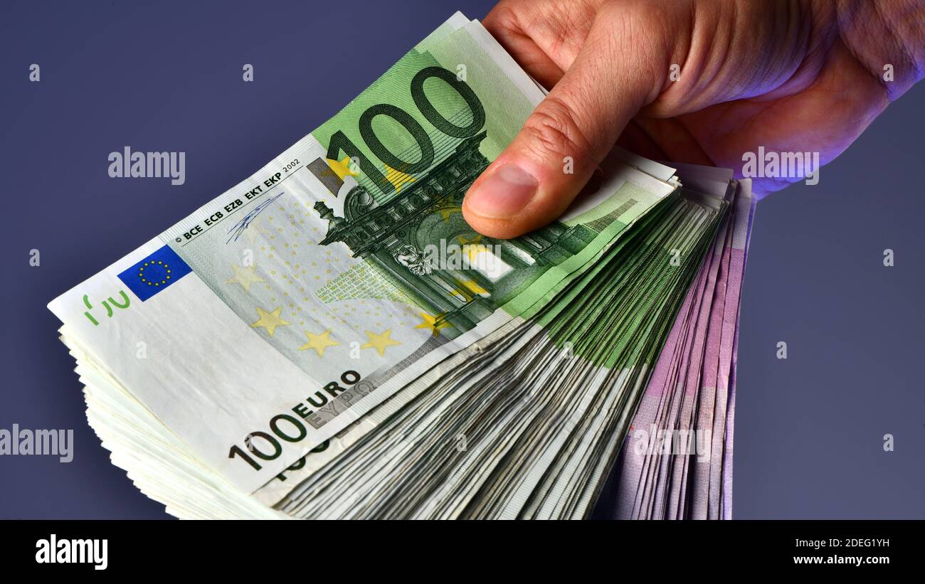 Une main d'homme montre 20,000 euros en billets de 100 euros et 500 euros sur fond bleu. Acheter une nouvelle voiture Banque D'Images