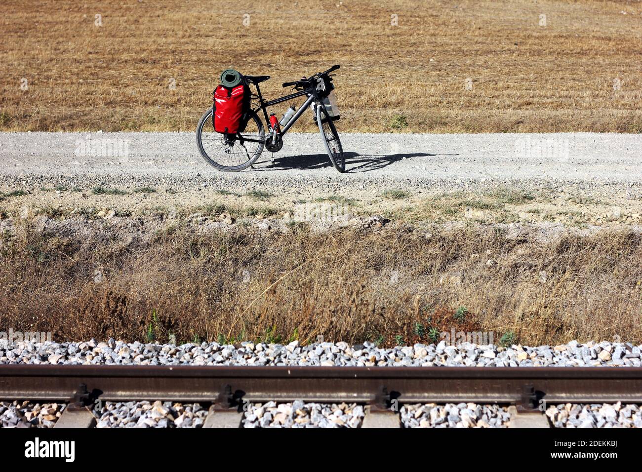 Vélo chargé d'équipement de randonnée et de camping stationné sur le côté de la route asphaltée dans la nature sous ciel clair à l'extérieur. Chemins de fer en face. Banque D'Images