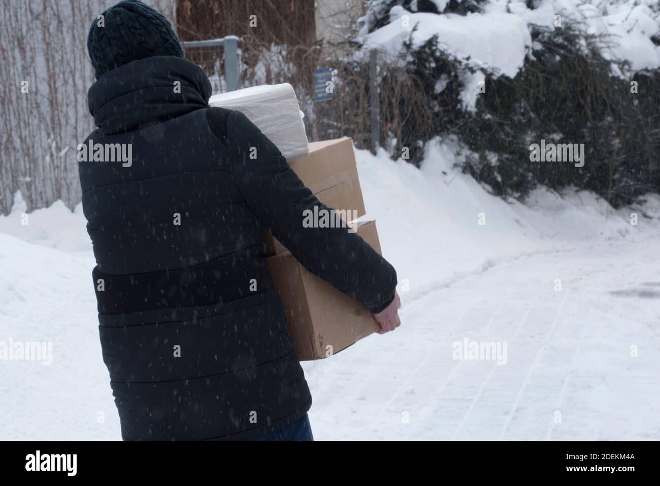 personne portant une veste d'hiver et une casquette noires pour livrer les paquets dans l'hiver Banque D'Images