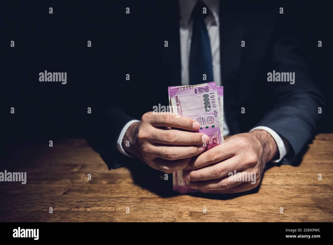 Homme d'affaires anonyme détenant de l'argent, monnaie de la roupie indienne, à la table dans une salle privée sombre - corruption, vénalité et concepts de corruption Banque D'Images