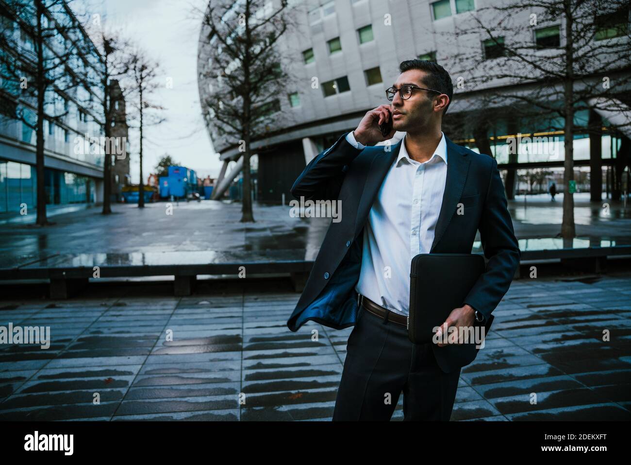 Homme d'affaires de course mixte portant un costume parlant sur un appareil cellulaire bâtiment de bureau extérieur Banque D'Images