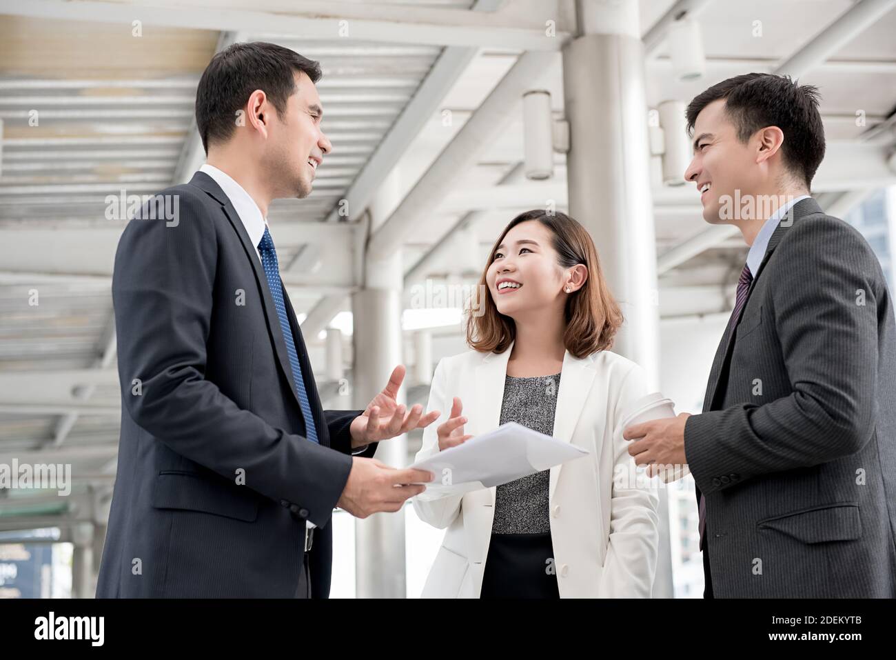 Des collaborateurs asiatiques heureux se réunissent à l'extérieur du bureau avec un café et des documents traitant du travail Banque D'Images
