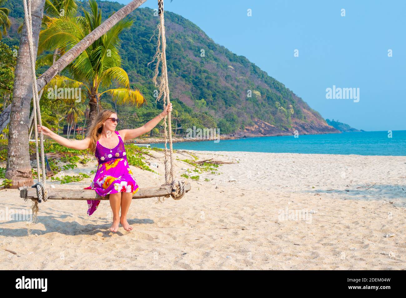 Femme européenne, blonde aux cheveux longs dans une robe brillante balançant sur une balançoire sur la mer. Voyages et tourisme en Asie. Copie de l'espace. Banque D'Images