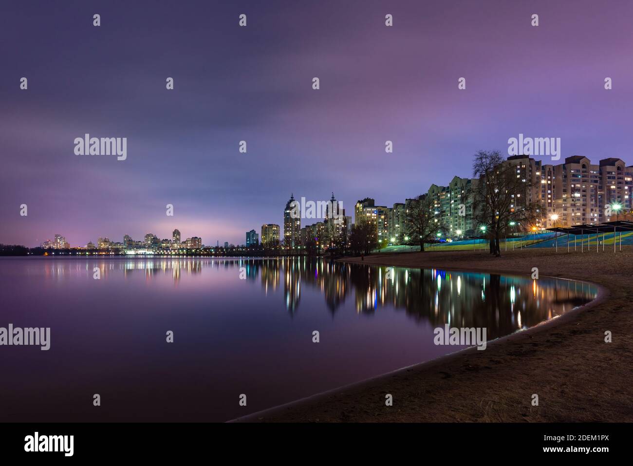 Vue nocturne des bâtiments modernes dans le quartier Obolon de Kiev, Ukraine, près du fleuve Dnieper, les lumières se reflètent sur l'eau calme. Banque D'Images